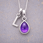 sterling Silver necklace with a 'L' initial pendant and a purple teardrop february birthstone amethyst pendant on a textured grey background