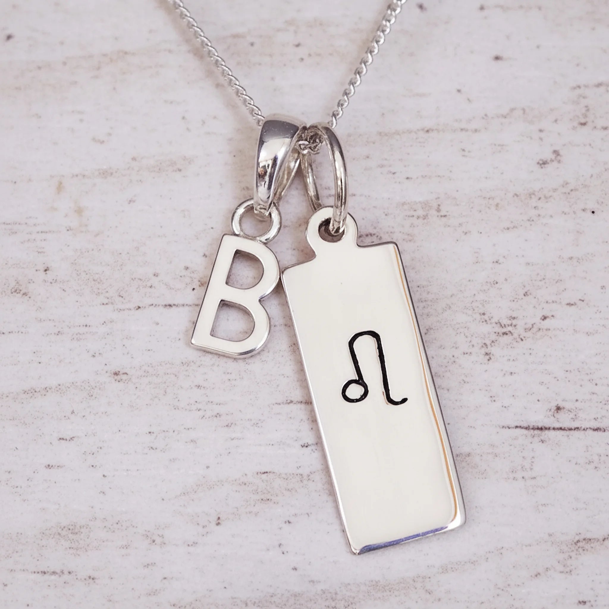 Sterling Silver chain necklace with a Leo Zodiac Star Sign pendant and a initial 'B' letter pendant on a wooden background.