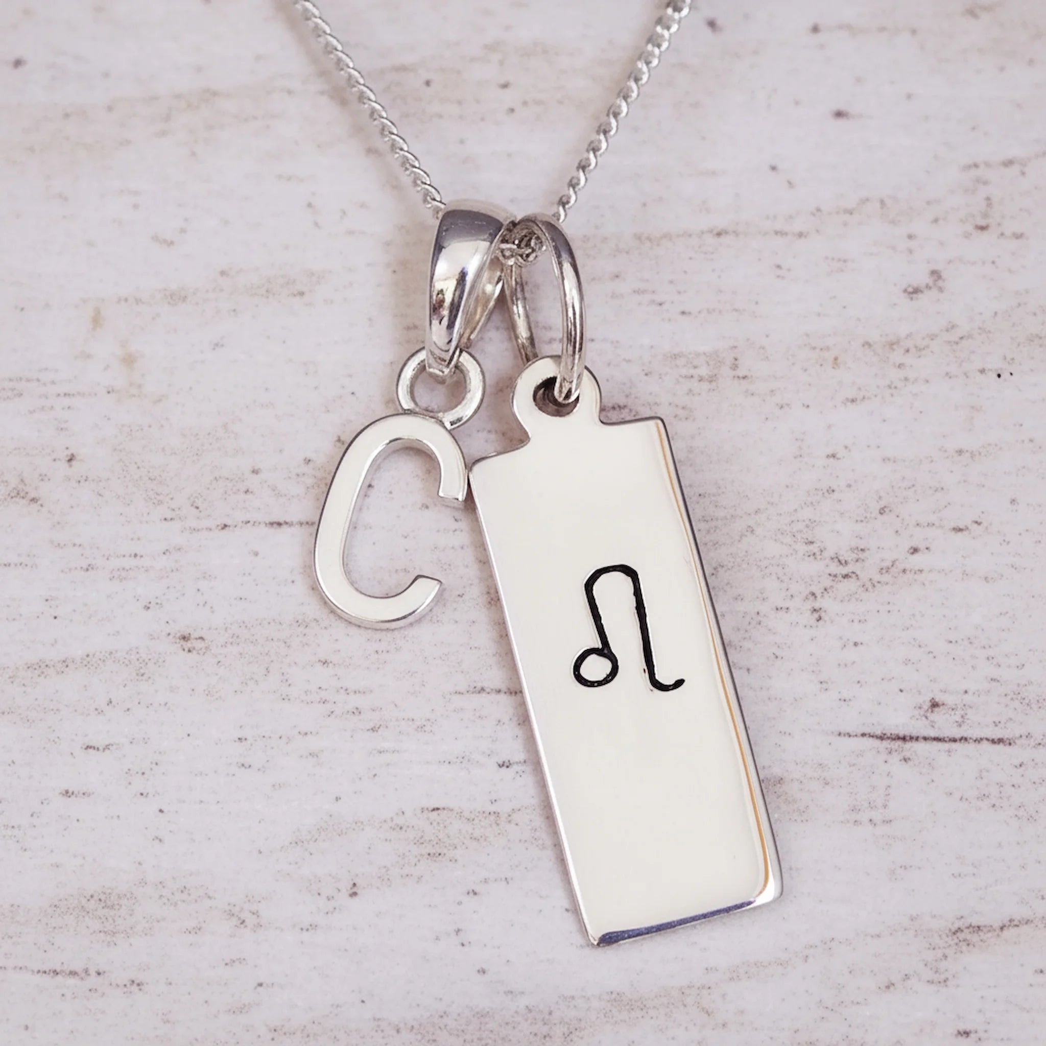 Sterling Silver necklace with a Leo Zodiac Star Sign pendant and a initial 'C' letter pendant on a light wooden background.
