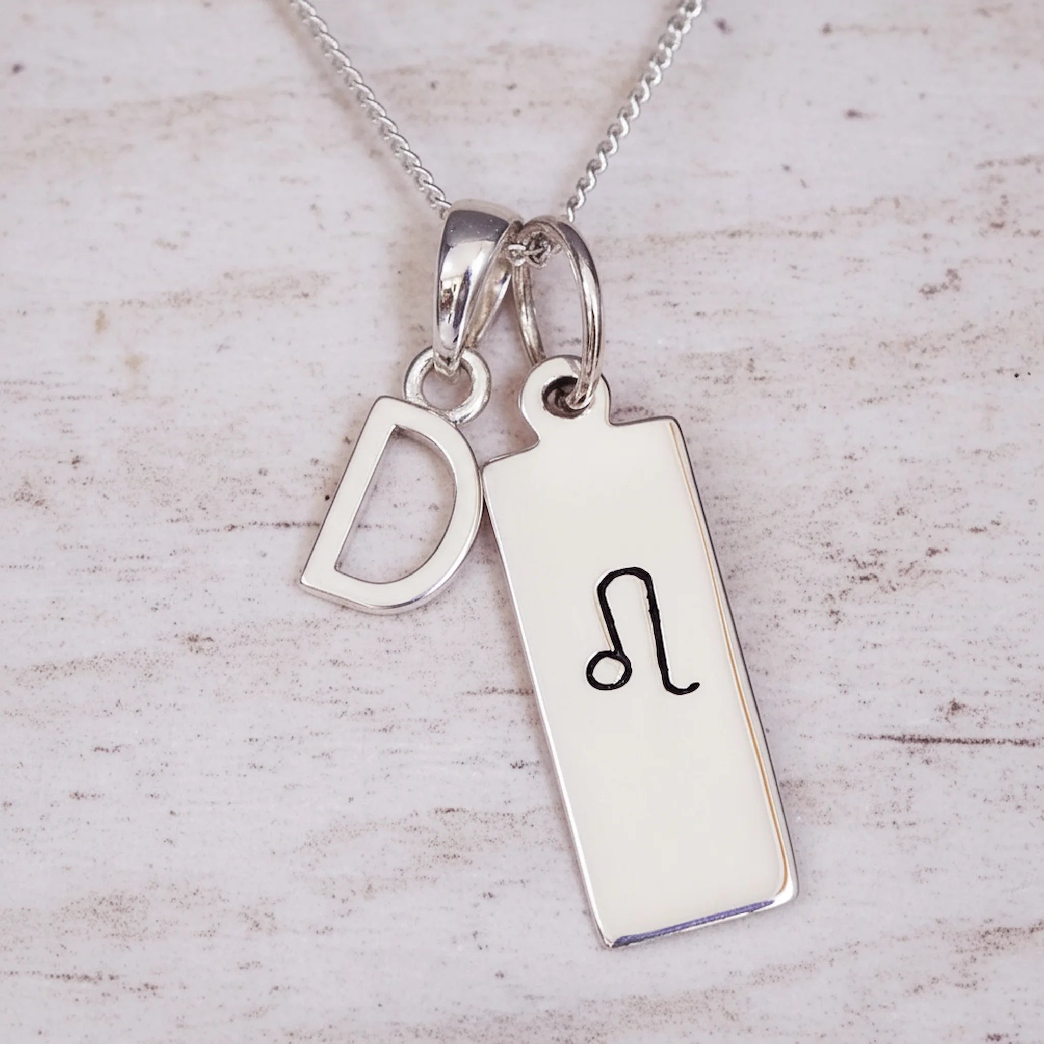 Sterling Silver necklace with a Leo Zodiac Star Sign pendant and a initial 'D' letter pendant on a light wooden background.