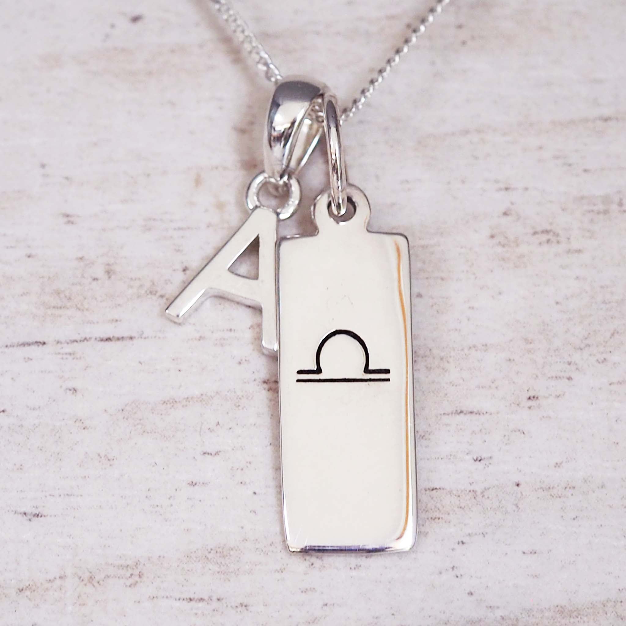 sterling Silver necklace with a libra zodiac pendant and a 'A' initial pendant on a light wooden background