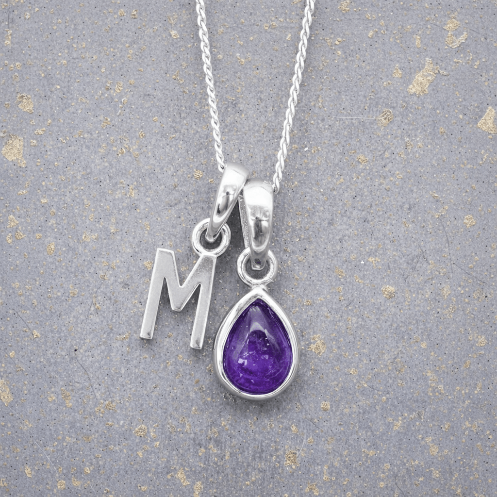 sterling Silver necklace with a purple teardrop february birthstone amethyst pendant and letter 'M' charm on a textured grey background.