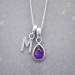 sterling Silver necklace with a purple teardrop february birthstone amethyst pendant and letter 'M' charm on a textured grey background.