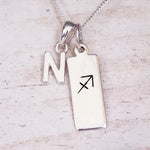Sterling silver initial N and Sagittarius zodiac bar necklace, close-up of the letter charm and pendant on whitewashed wood
