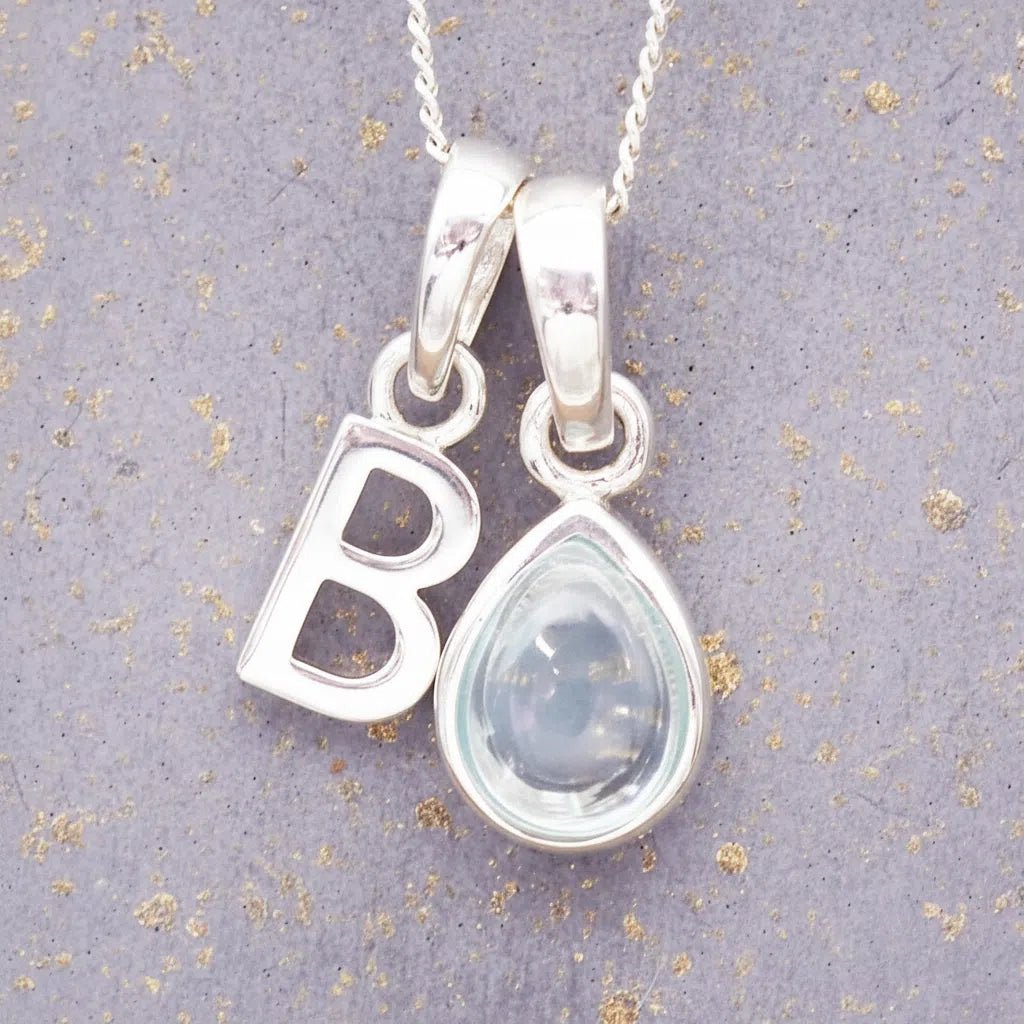 sterling silver 'B' initial necklace with tear drop november birthstone topaz gemstone on a grey background.