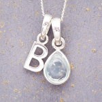 sterling silver 'B' initial necklace with tear drop november birthstone topaz gemstone on a grey background.