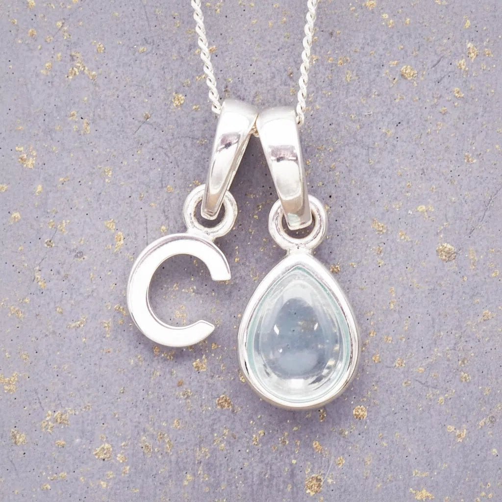 sterling silver 'C' initial necklace with tear drop november birthstone topaz gemstone on a grey background.
