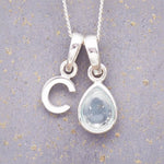 sterling silver 'C' initial necklace with tear drop november birthstone topaz gemstone on a grey background.