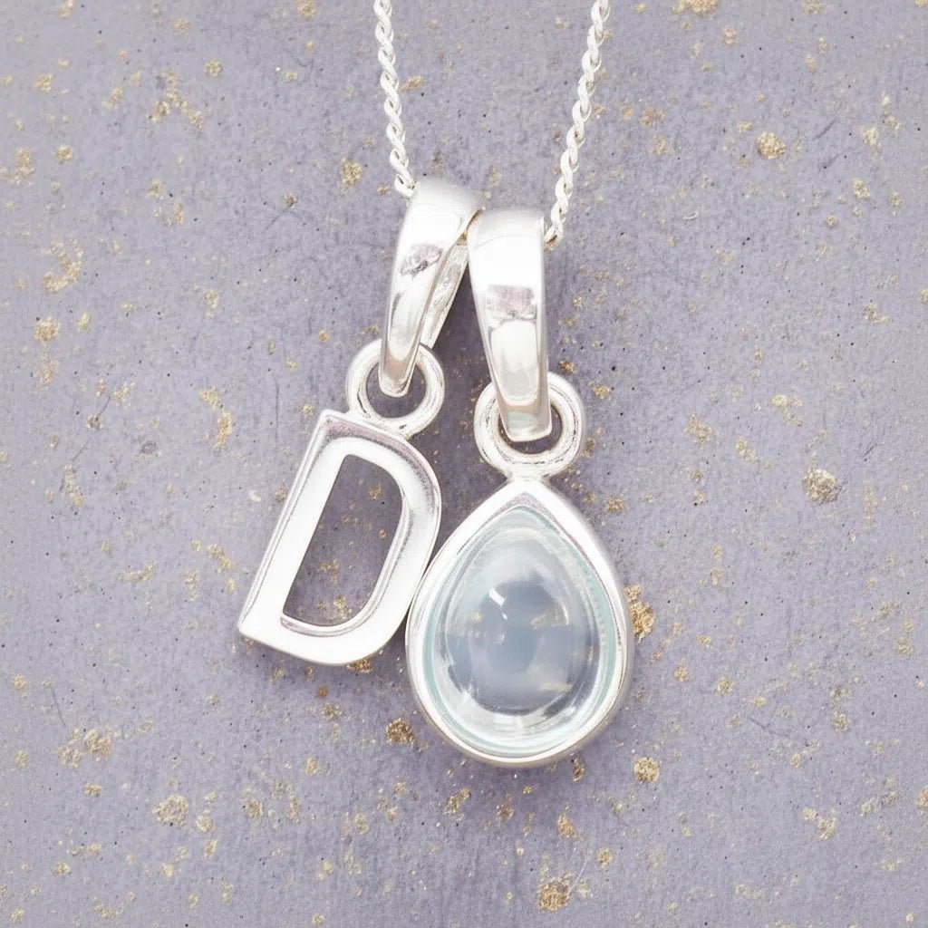sterling silver 'D' initial necklace with tear drop november birthstone topaz gemstone on a grey background.