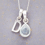 sterling silver 'D' initial necklace with tear drop november birthstone topaz gemstone on a grey background.