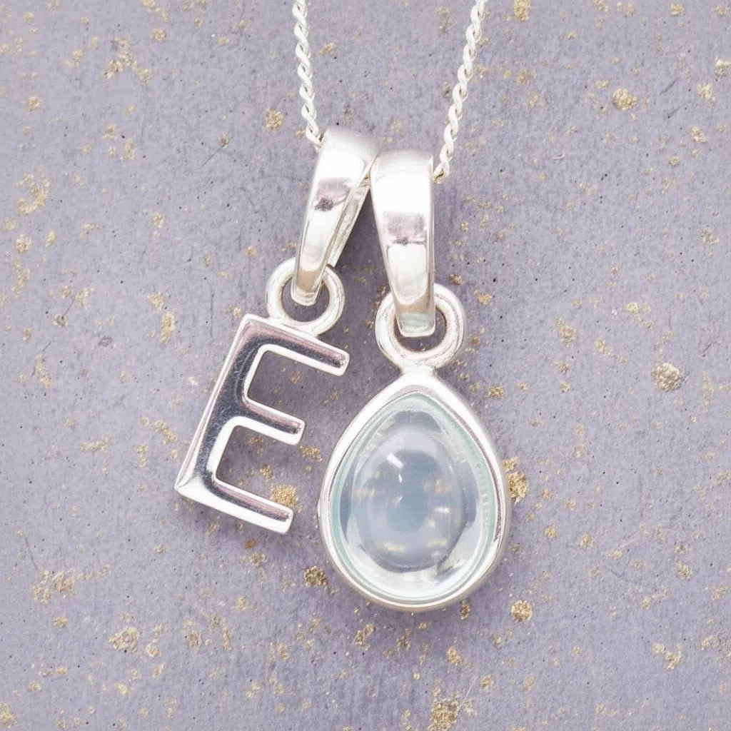 sterling silver 'E' initial necklace with tear drop november birthstone topaz gemstone on a grey background.