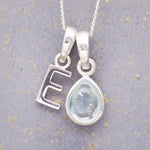 sterling silver 'E' initial necklace with tear drop november birthstone topaz gemstone on a grey background.
