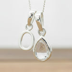 Silver Initial O necklace with a teardrop-shaped Herkimer Quartz crystal pendant hanging above a rustic wooden surface