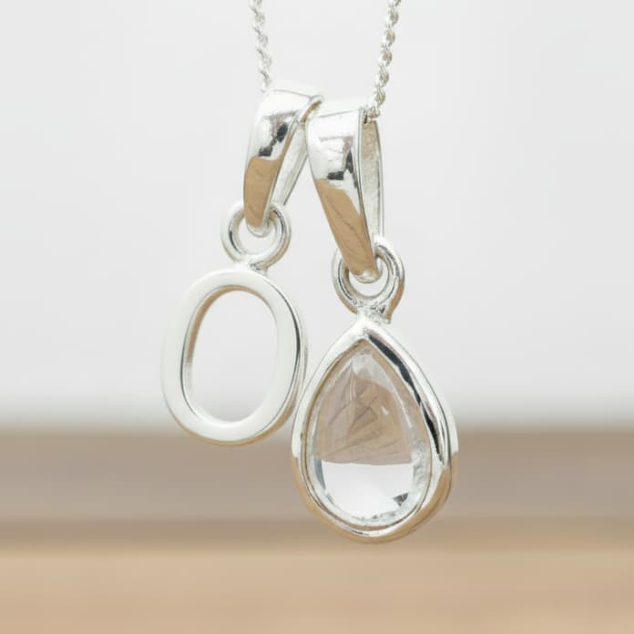 Silver Initial O necklace with a teardrop-shaped Herkimer Quartz crystal pendant hanging above a rustic wooden surface