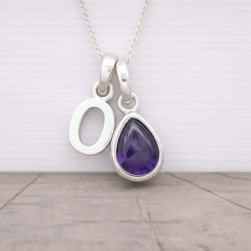 Silver initial O necklace with a purple teardrop amethyst pendant on a light wooden surface.