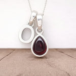 Silver Initial O necklace with a teardrop-shaped Garnet gemstone pendant hanging above a rustic wooden surface