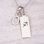 Sterling silver initial O and Sagittarius zodiac bar necklace, close-up of the letter charm and pendant on whitewashed wood