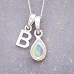 Silver necklace with 'B' pendant and teardrop-shaped opal pendant on a textured gray background.