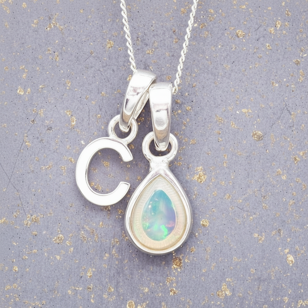 Sterling Silver necklace with a teardrop-shaped october birthstone opal pendant and a 'C' initial pendant on a textured grey background