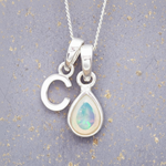 Sterling Silver necklace with a teardrop-shaped october birthstone opal pendant and a 'C' initial pendant on a textured grey background