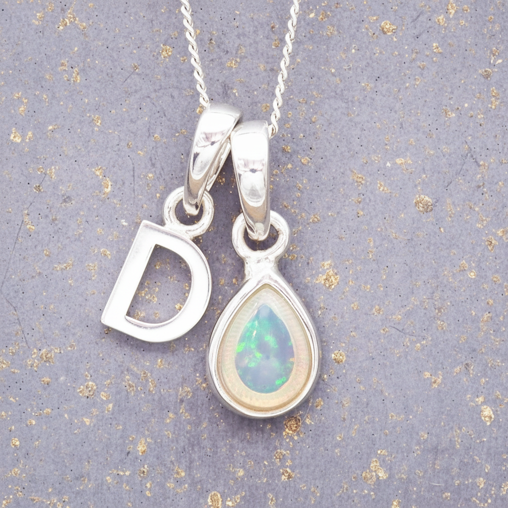 Silver necklace with 'D' pendant and teardrop-shaped opal pendant on a textured grey background.