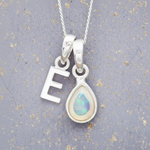 Silver necklace with 'E' pendant and teardrop-shaped opal pendant on a textured gray background.