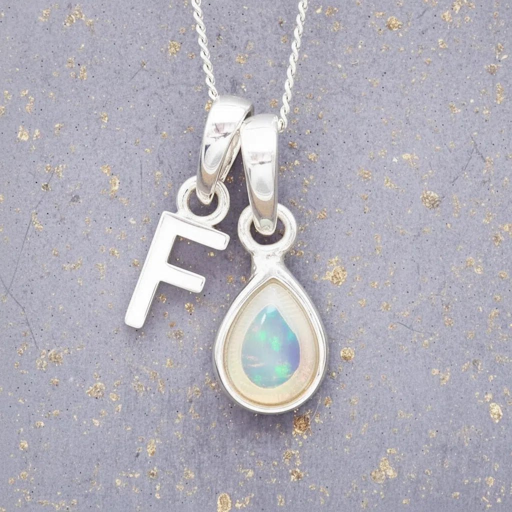Sterling Silver necklace with 'F' initial pendant and white teardrop October Birthstone Opal gemstone on a grey background.