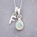 Sterling Silver necklace with 'F' initial pendant and white teardrop October Birthstone Opal gemstone on a grey background.