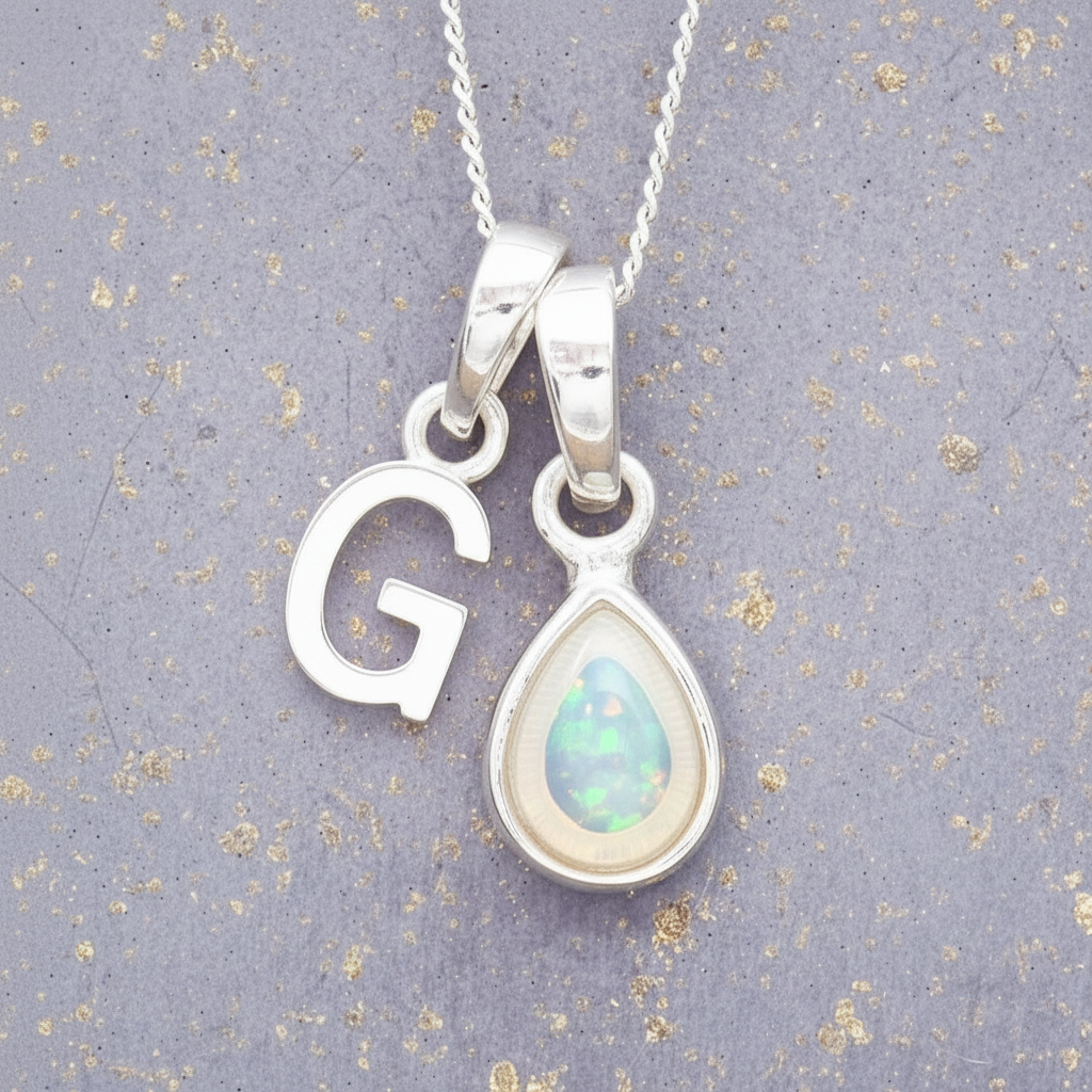 Silver necklace with 'G' pendant and teardrop-shaped opal pendant on a textured gray background