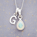 Silver necklace with 'G' pendant and teardrop-shaped opal pendant on a textured gray background