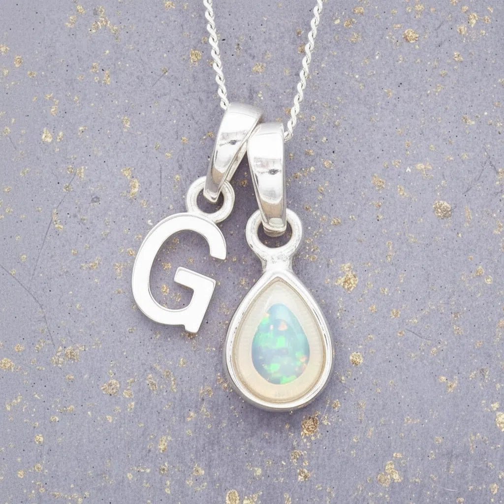 Sterling Silver necklace with 'G' initial pendant and white teardrop October Birthstone Opal gemstone on a grey background.