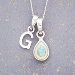 Sterling Silver necklace with 'G' initial pendant and white teardrop October Birthstone Opal gemstone on a grey background.