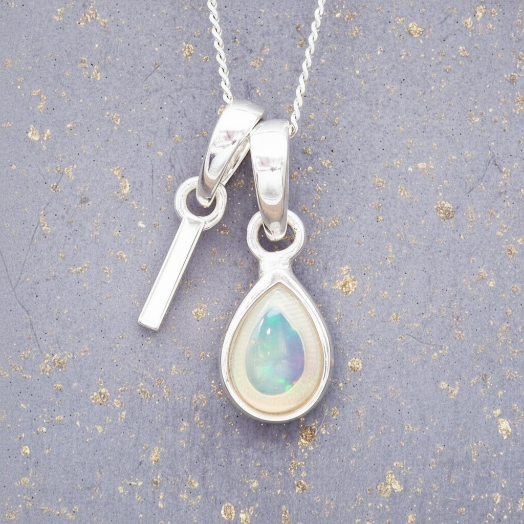 sterlingSilver necklace with a 'I' initial and a teardrop-shaped opal pendant on a textured grey background