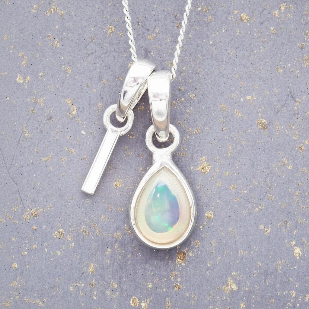 Sterling Silver necklace with 'I' initial pendant and white teardrop October Birthstone Opal gemstone on a grey background.