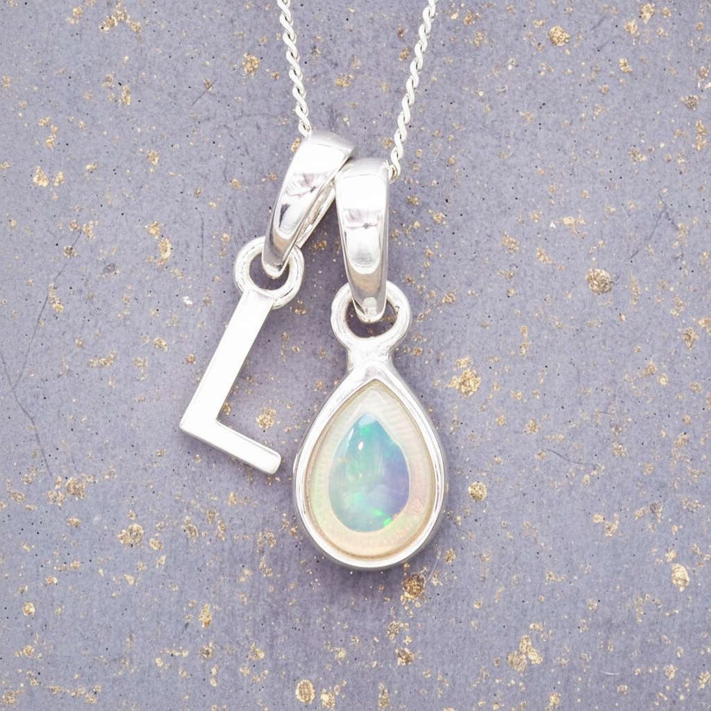 Silver necklace with a teardrop-shaped october birthstone opal pendant and a 'L'initial pendant on a textured grey background