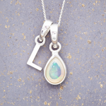 Silver necklace with a teardrop-shaped october birthstone opal pendant and a 'L'initial pendant on a textured grey background
