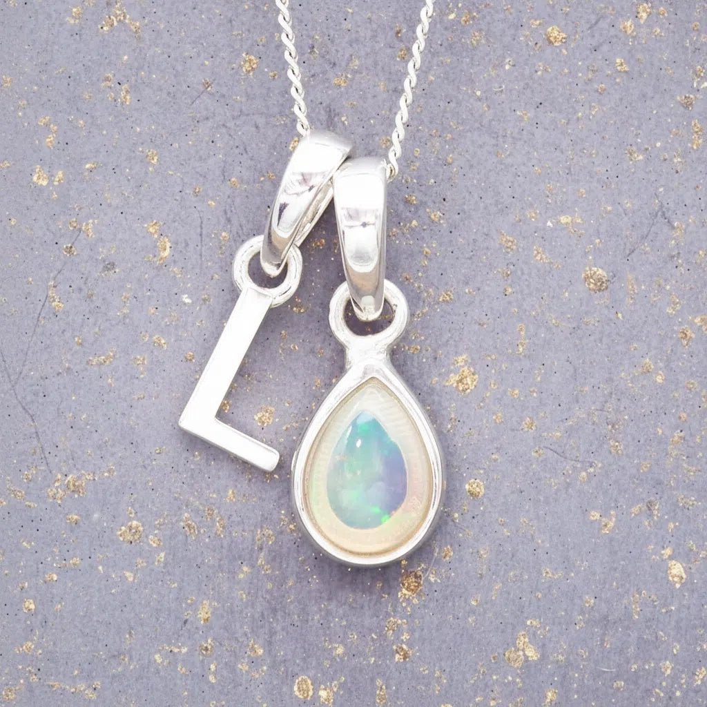 Sterling Silver necklace with 'L' initial pendant and white teardrop October Birthstone Opal gemstone on a grey background.