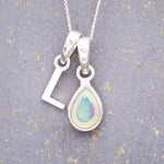 Sterling Silver necklace with 'L' initial pendant and white teardrop October Birthstone Opal gemstone on a grey background.
