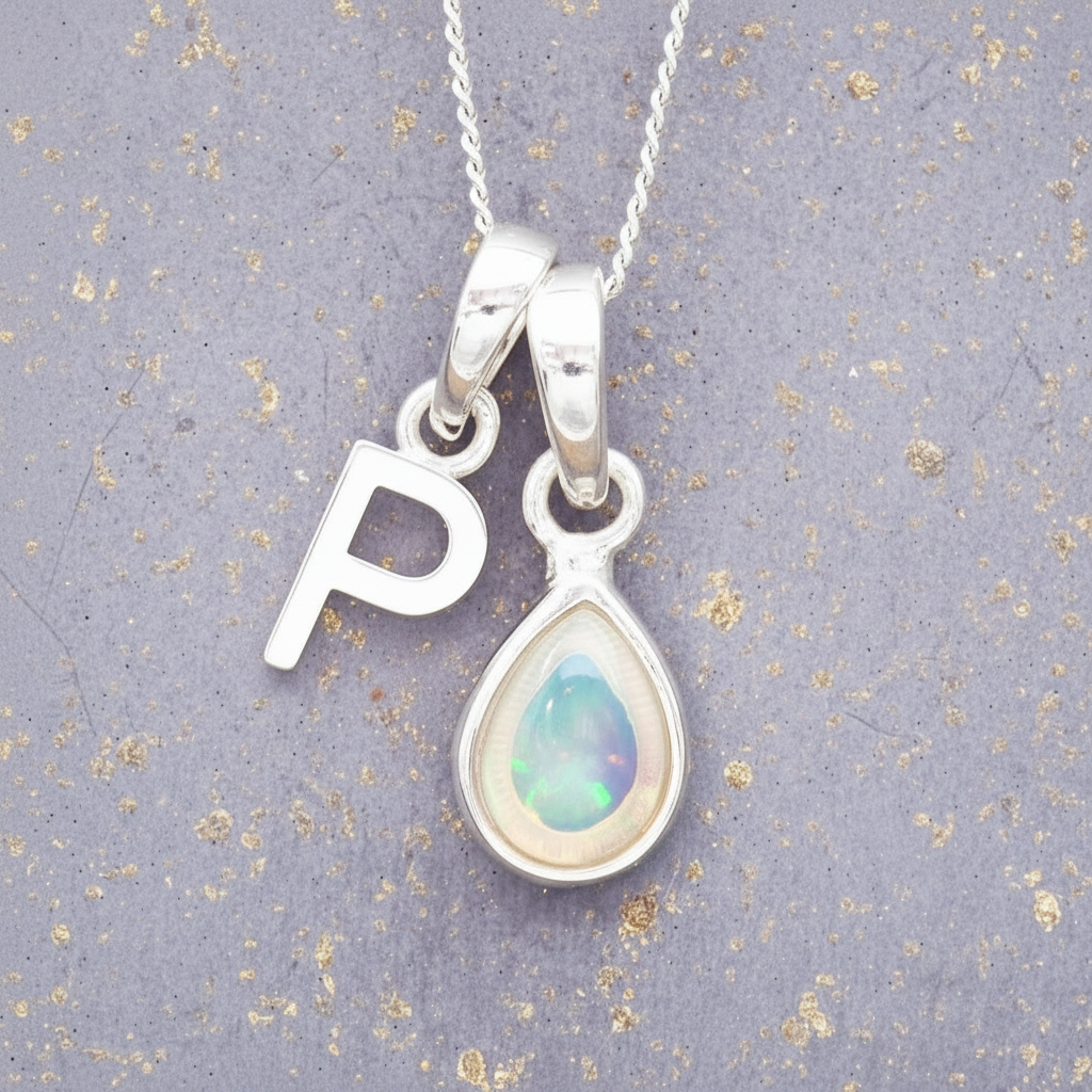 Silver necklace with a 'P' pendant and a teardrop-shaped opal stone on a textured gray background.