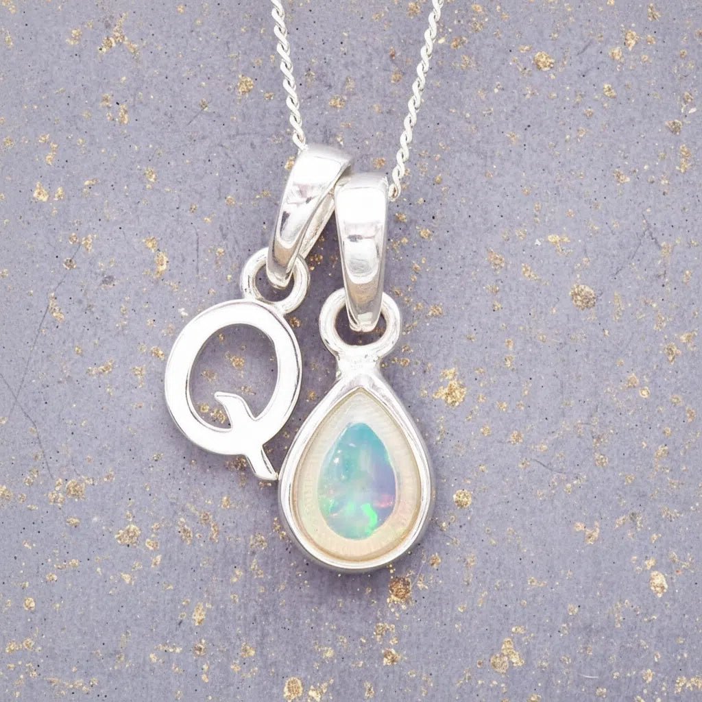 Sterling Silver necklace with 'Q' initial pendant and white teardrop October Birthstone Opal gemstone on a grey background.