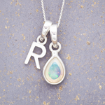 Silver necklace with 'R' pendant and teardrop-shaped opal pendant on a textured grey background.