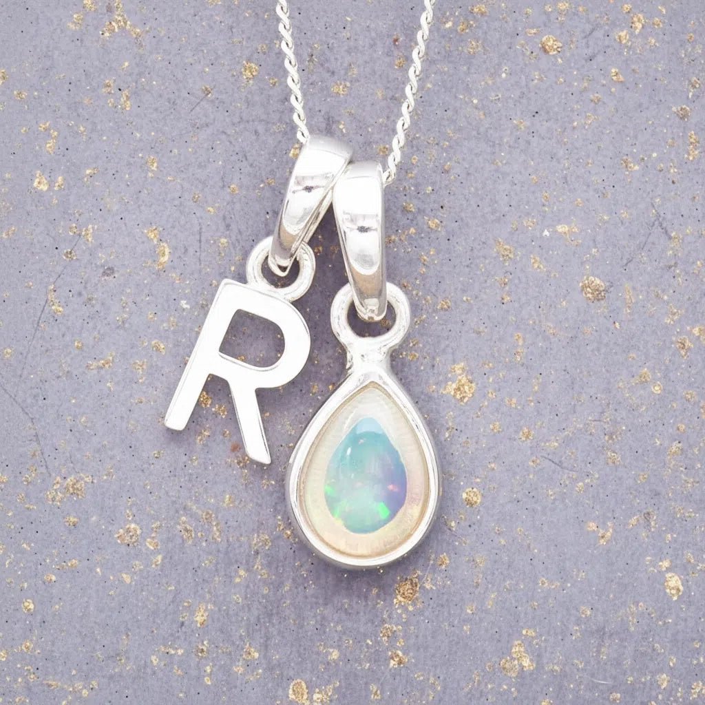 Sterling Silver necklace with 'R' initial pendant and white teardrop October Birthstone Opal gemstone on a grey background.
