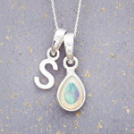 Sterling Silver necklace with a teardrop-shaped october birthstone opal pendant and a 'S' initial pendant on a textured grey background.