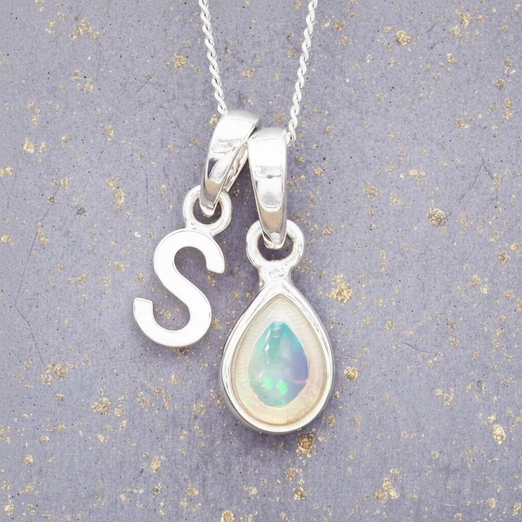 Sterling Silver necklace with 'S' initial pendant and white teardrop October Birthstone Opal gemstone on a grey background.