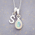 Sterling Silver necklace with 'S' initial pendant and white teardrop October Birthstone Opal gemstone on a grey background.