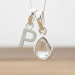 Silver Initial P necklace with a teardrop-shaped Herkimer Quartz crystal pendant hanging above a rustic wooden surface