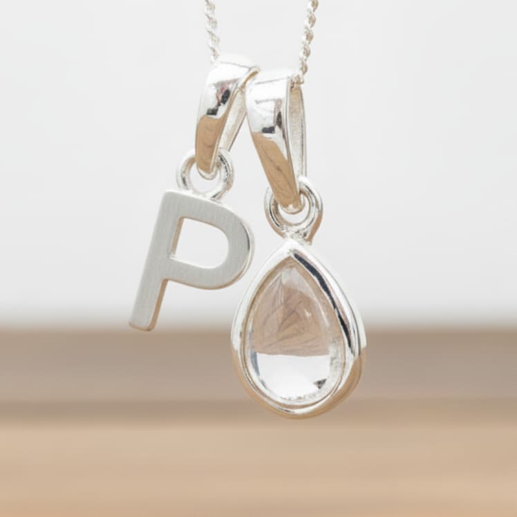 Silver Initial P necklace with a teardrop-shaped Herkimer Quartz crystal pendant hanging above a rustic wooden surface