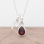 Silver initial P necklace with a teardrop-shaped garnet gemstone pendant on a wood surface.