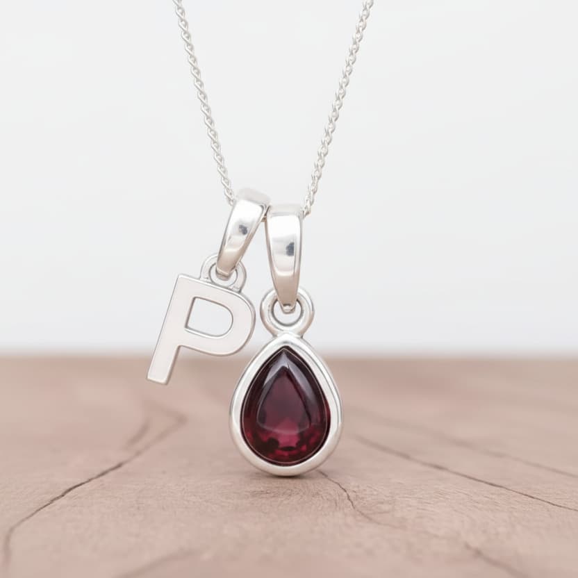 Silver initial P necklace with a teardrop-shaped garnet gemstone pendant on a wood surface.