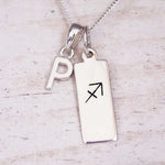 Sterling silver initial P and Sagittarius zodiac bar necklace, close-up of the letter charm and pendant on whitewashed wood